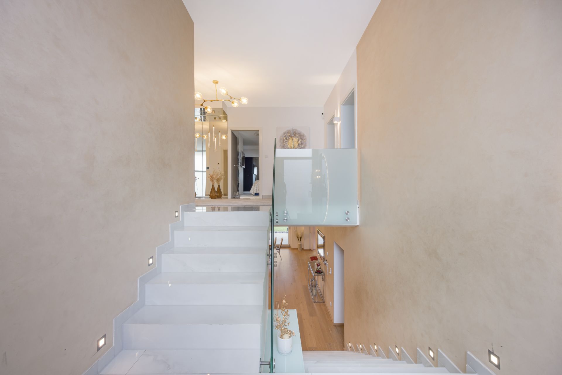 Weiße Treppe mit Glasgeländer und beigen Wänden in einem modernen Wohnhaus.