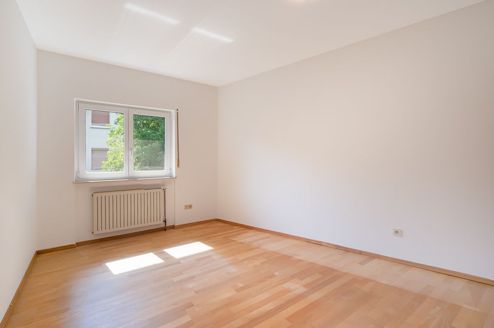 Leerer Raum mit Parkettboden, weißer Wand, Fenster und Heizkörper.