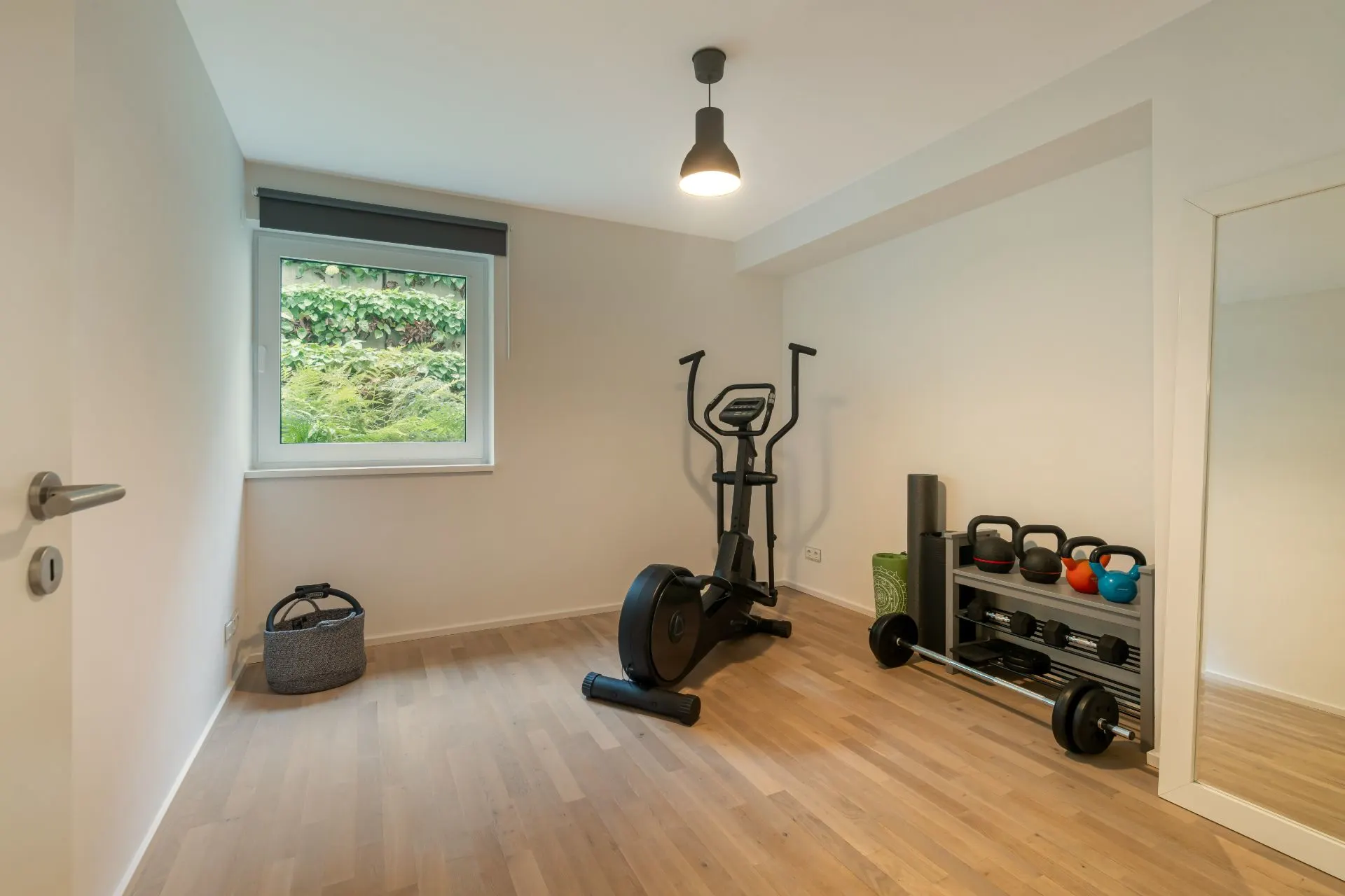 Helles Fitnesszimmer mit Heimtrainer, Hanteln, Yogamatte und großem Spiegel.