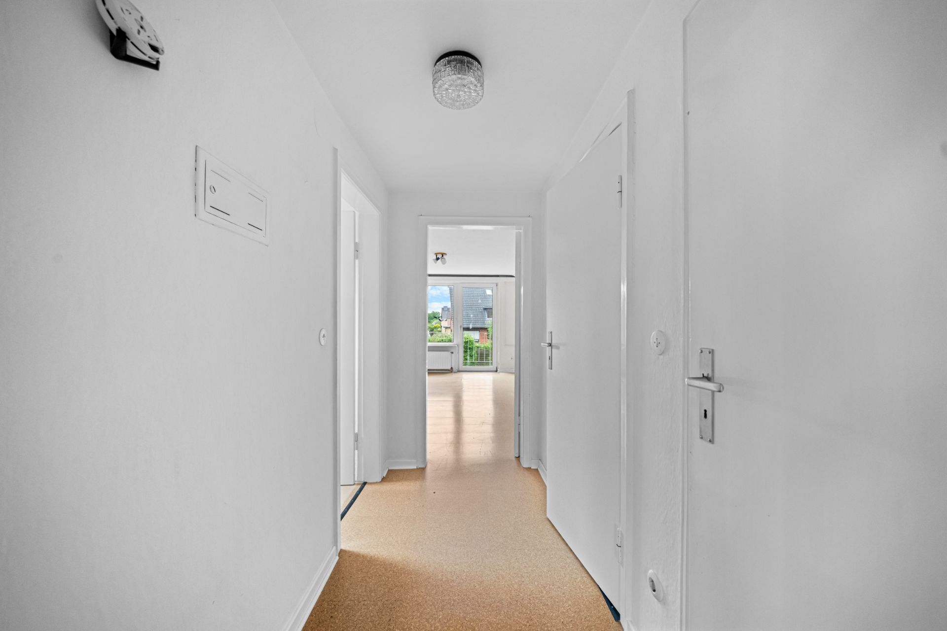 Heller Flur mit Türen und Blick in ein Zimmer mit Fenster und Balkon.