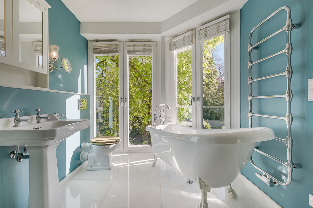 Helles Badezimmer mit freistehender Badewanne, Waschbecken, WC und großen Fenstern.
