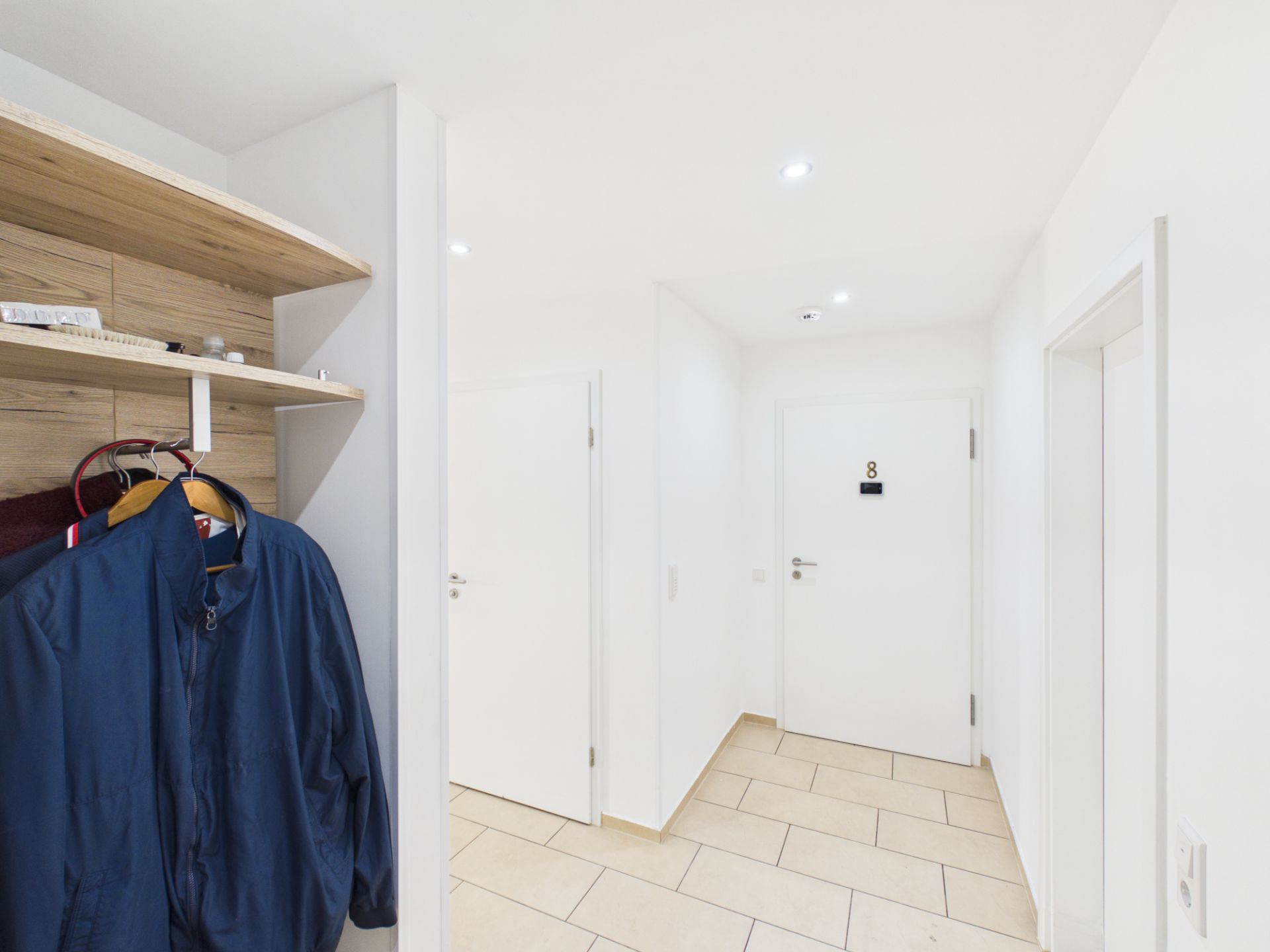 Heller Flur mit Garderobe, Jacken an Haken und mehreren weißen Türen.