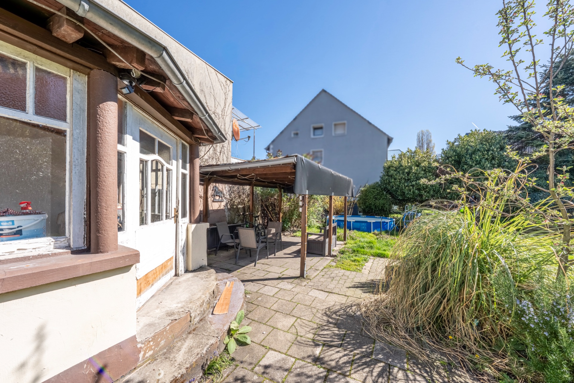 Wohnhaus mit Terrasse, überdachten Sitzbereich und Garten, im Hintergrund Aufstellpool.