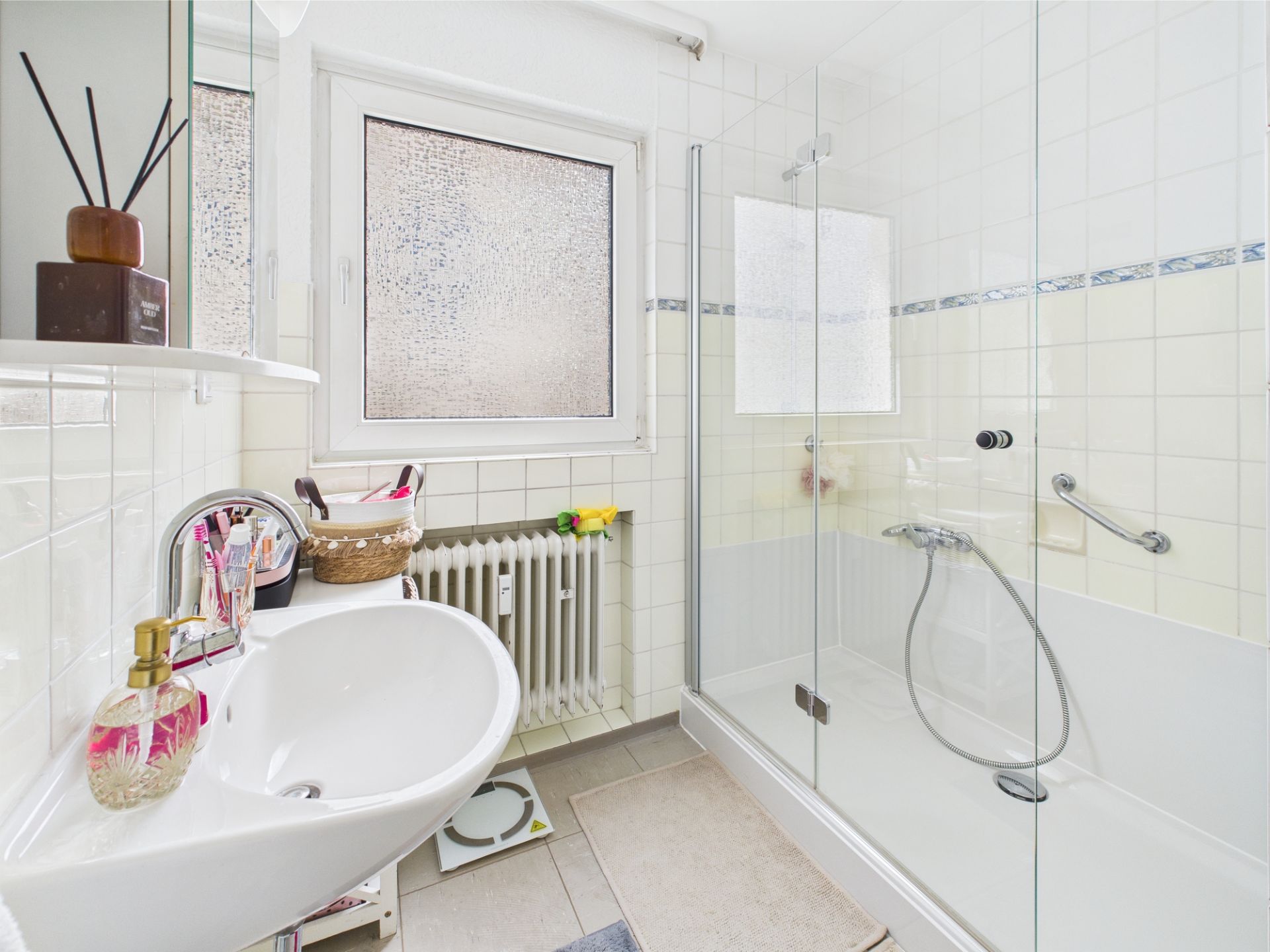 Helles Badezimmer mit Waschbecken, Fenster und großer Dusche mit Glastür.