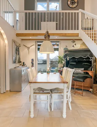 Essbereich mit Holztisch, sechs Stühlen und einer hölzernen Treppe in einem offenen, hellen Raum.