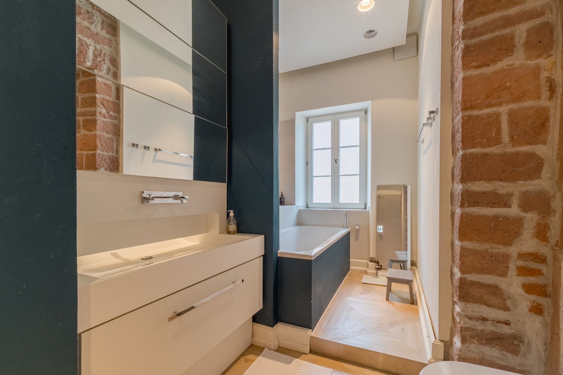 Modernes Badezimmer mit Waschbecken, Badewanne, Fenster und Backsteinwand.