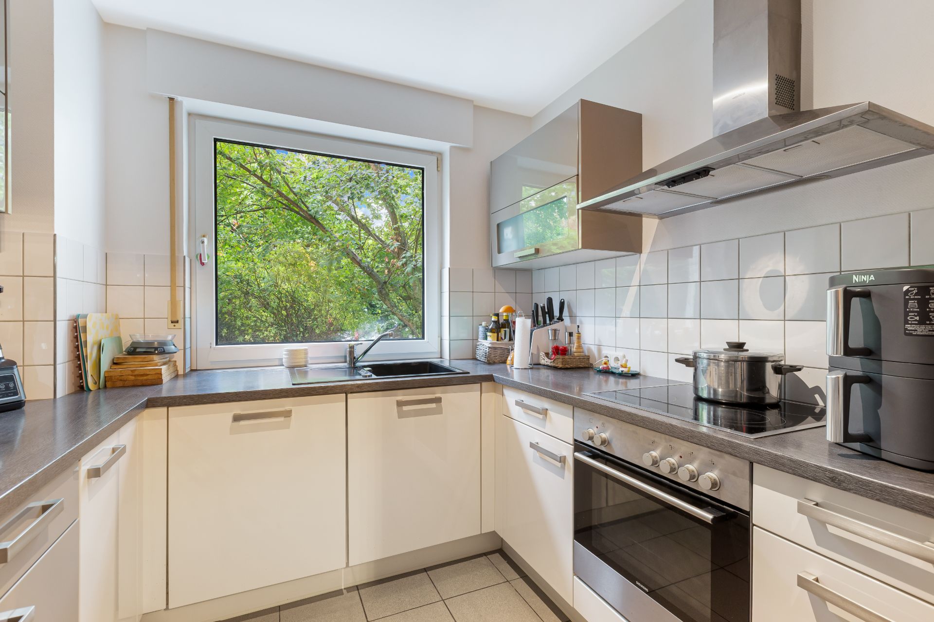 Moderne Küche mit weißen Schränken, Herd, großem Fenster und Blick ins Grüne.