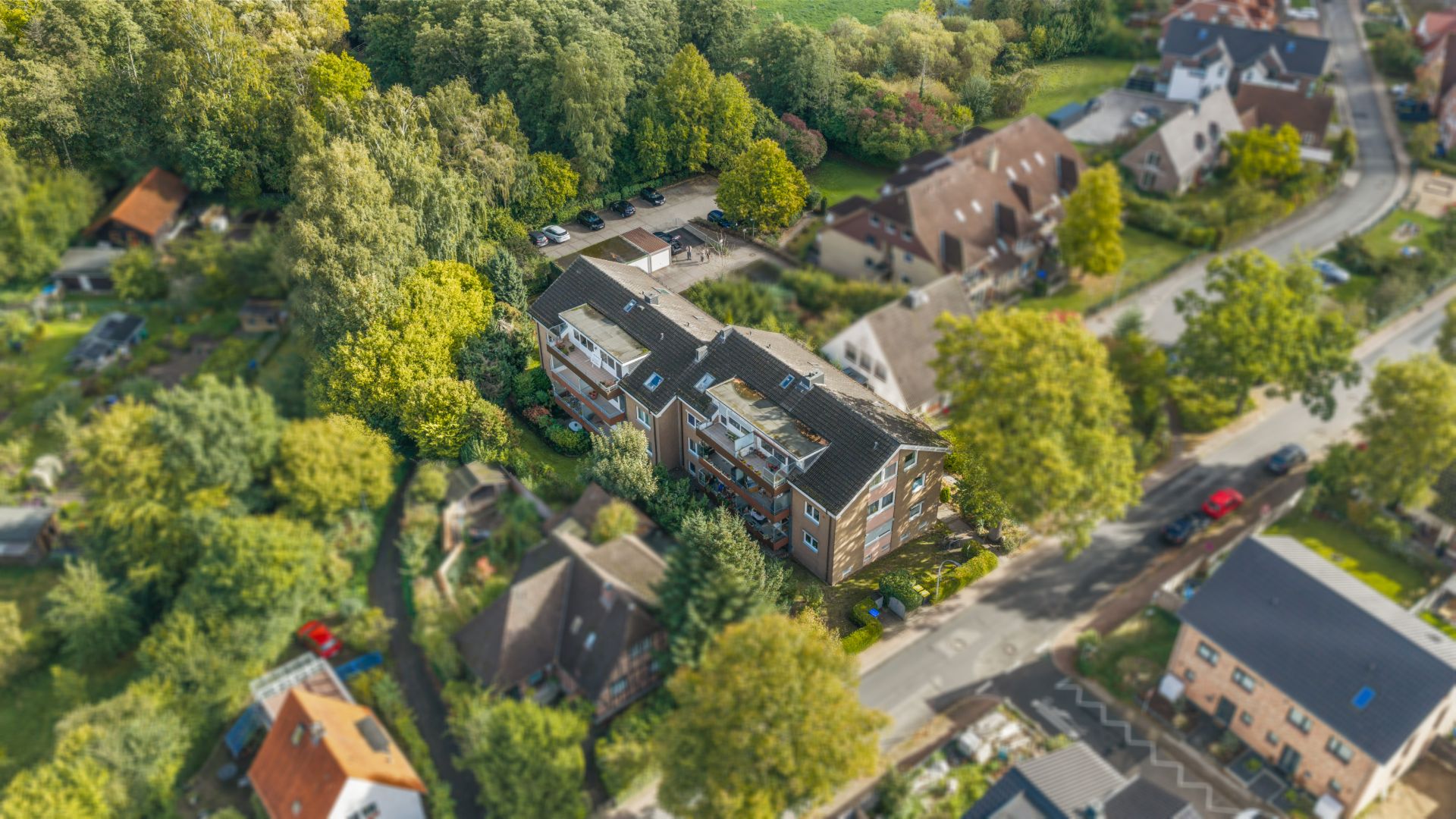Luftaufnahme eines Mehrfamilienhauses mit umliegenden Bäumen und Straßen.