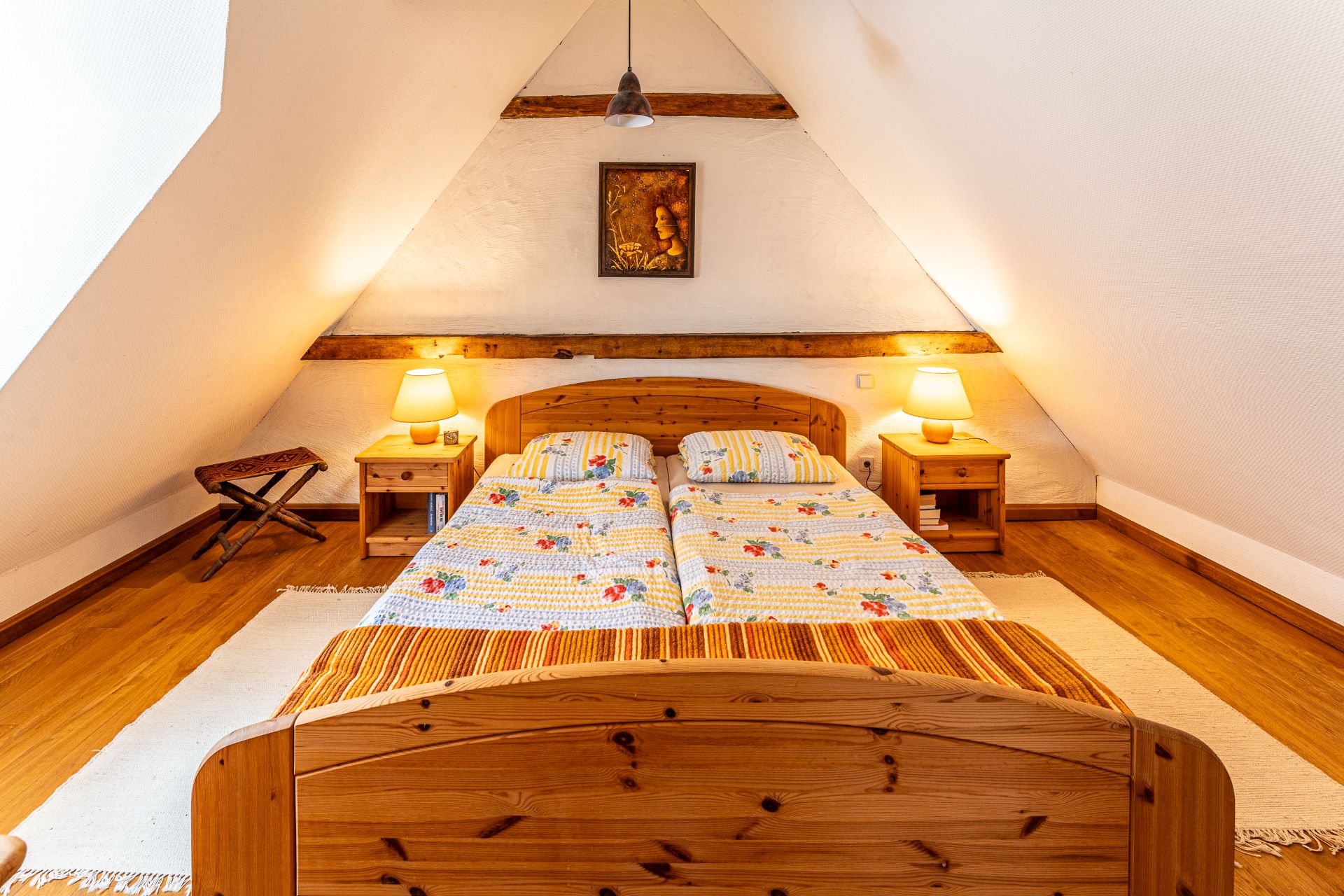 Gemütliches Schlafzimmer mit Holzbett, zwei Nachttischen, Lampen und schrägem Dach.