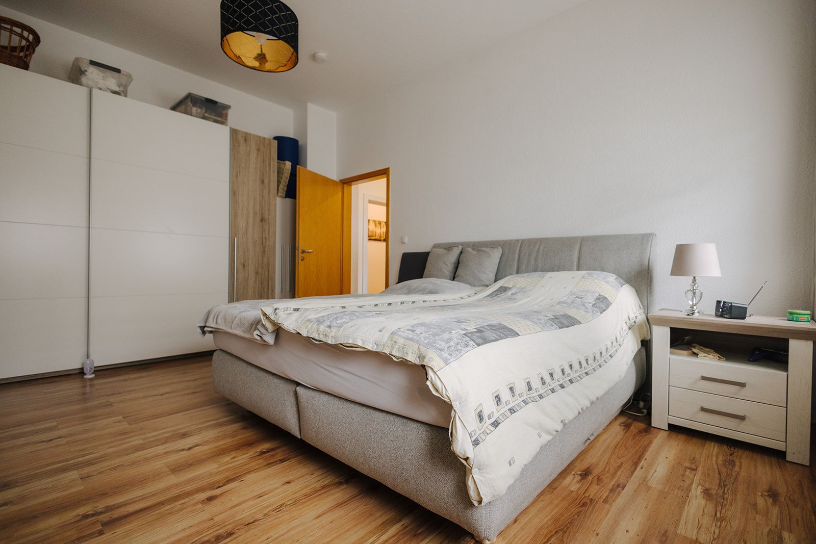 Schlafzimmer mit großem Bett, Nachttisch, Kleiderschrank und Holzfußboden.