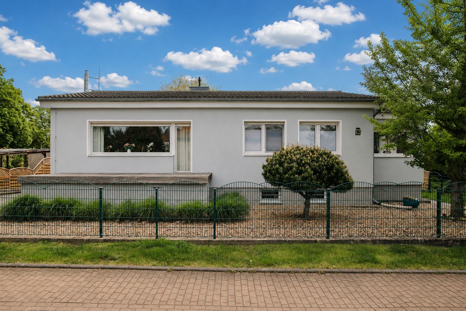Ein einstöckiges, weißes Wohnhaus mit großem Fenster, Garten und Zaun davor.