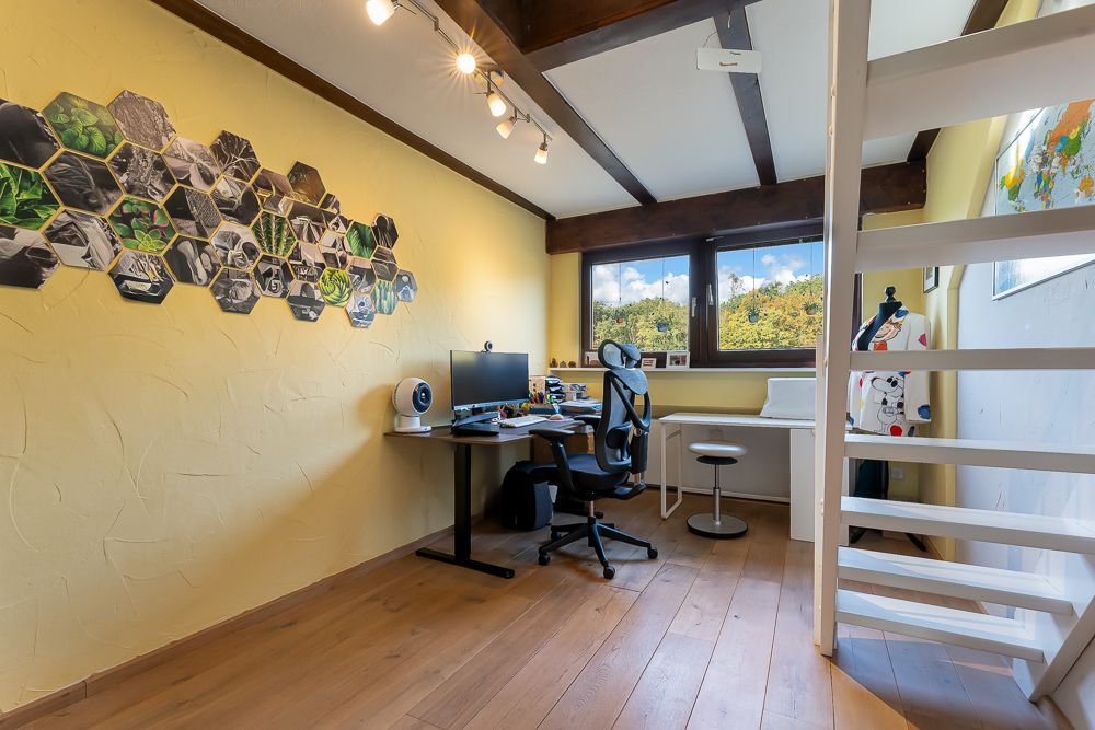 Helles Arbeitszimmer mit Schreibtisch, Computer, Stuhl, Wanddeko und Fenster, Treppe rechts.