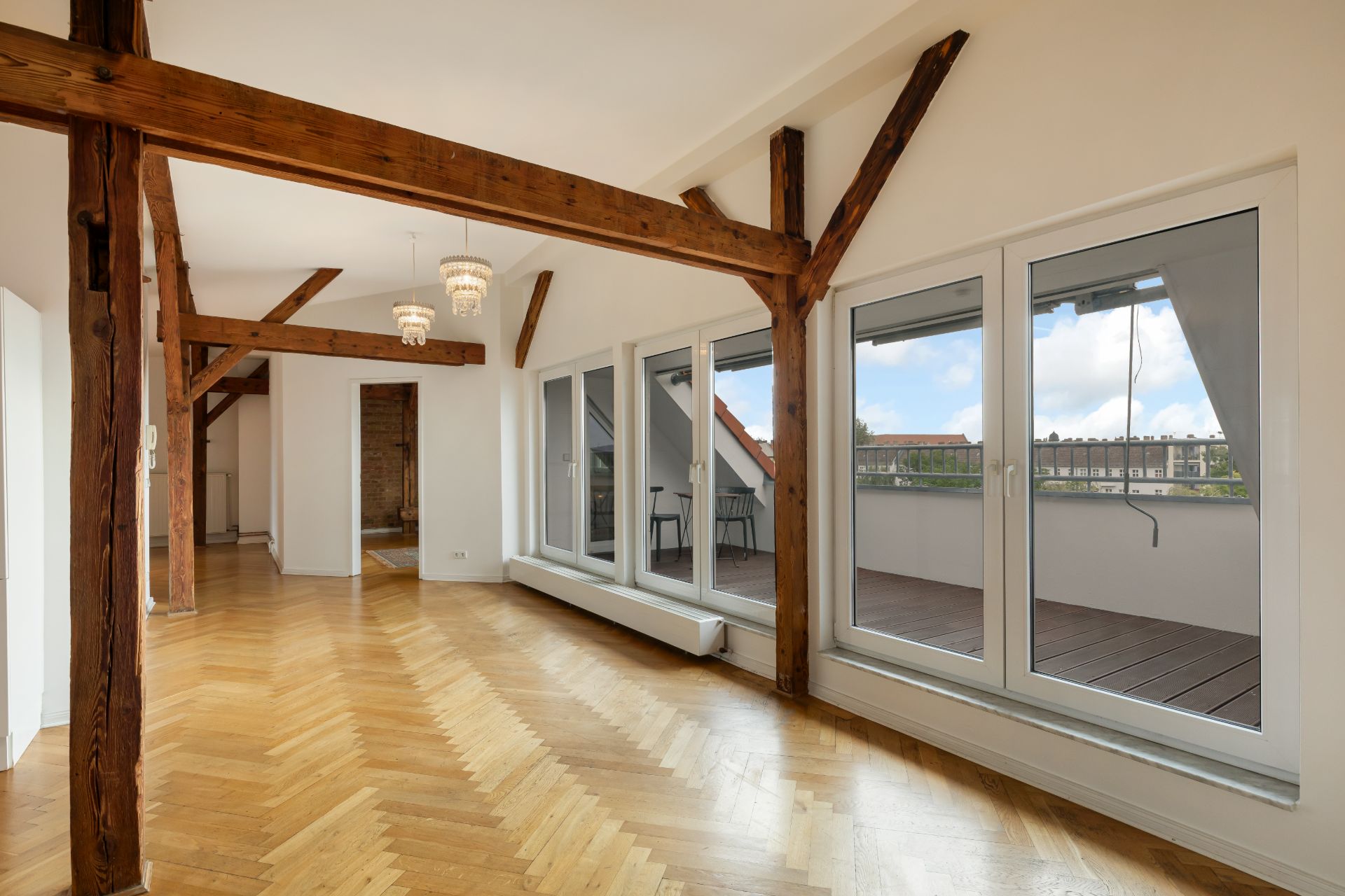 Helles Wohnzimmer mit Holzbalken, Parkettboden und großen Fenstern zu einem Balkon.