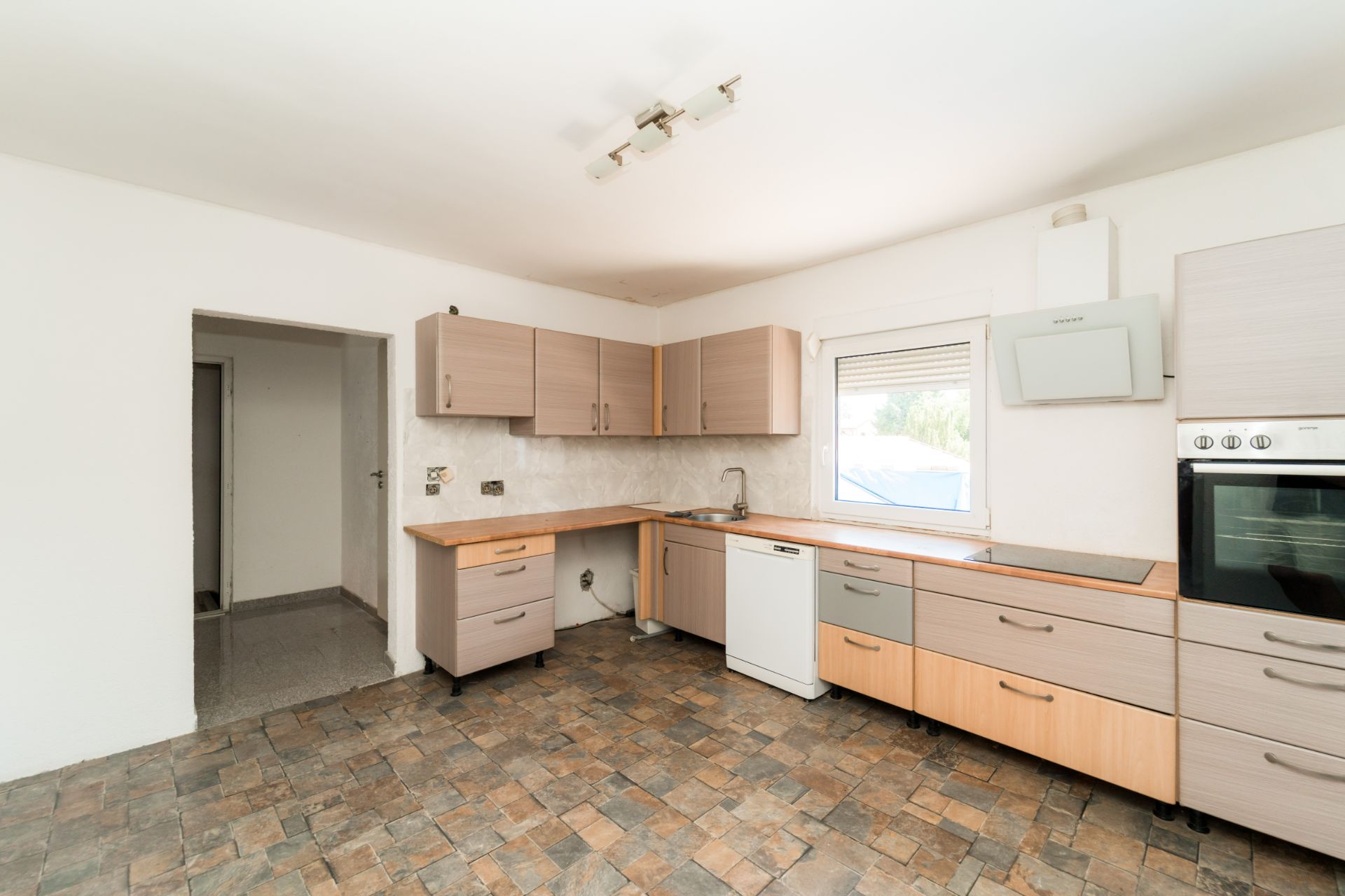Moderne, leere Küche mit Holzfronten, Einbauherd, Spüle, Geschirrspüler und Fenster.