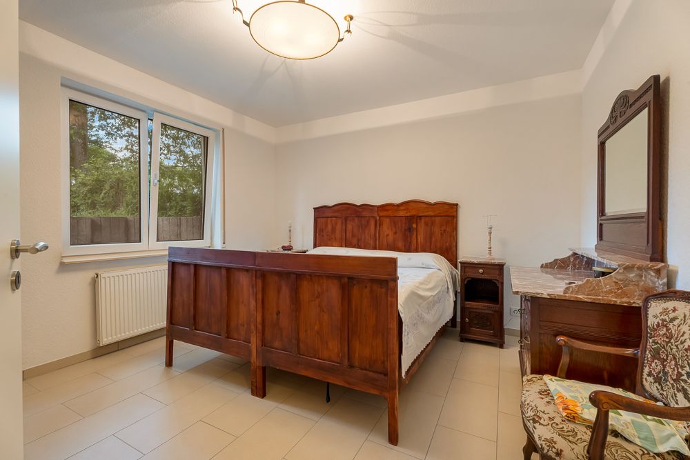 Schlafzimmer mit Holz-Doppelbett, Nachttisch, Kommode mit Spiegel und Stuhl.