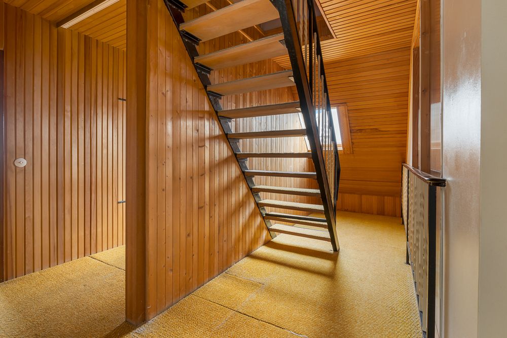 Treppenhaus mit Holzvertäfelung und gelbem Teppichboden, Fenster im Hintergrund.
