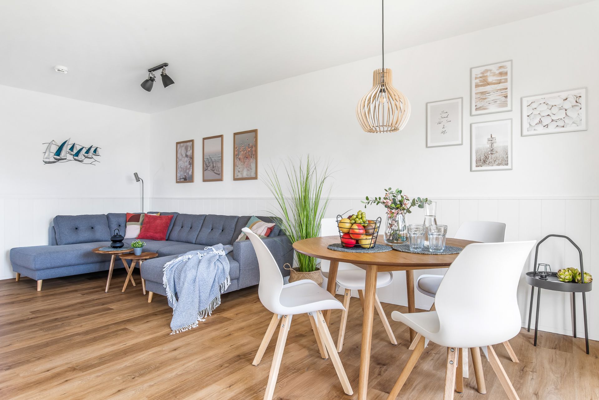 Helles Wohnzimmer mit grauem Sofa, rundem Esstisch, vier Stühlen und dekorativen Bildern an der Wand.