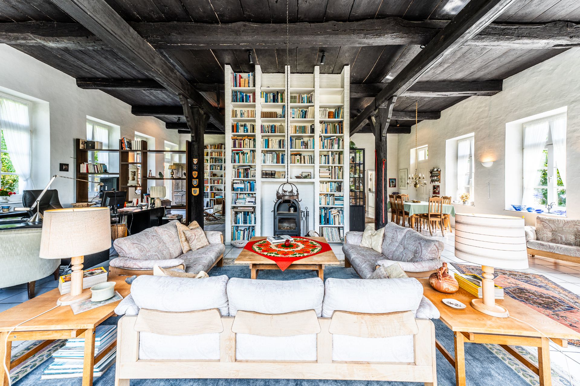 Helles Wohnzimmer mit Sofas, Holzdecke, großem Bücherregal und Kamin in der Mitte.