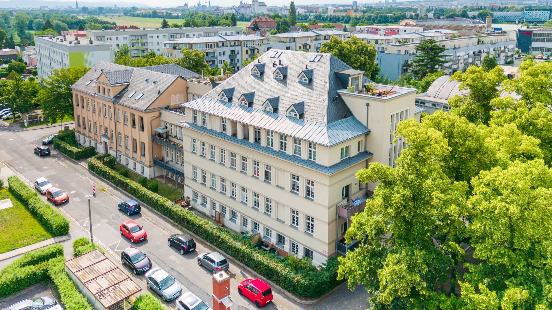 Mehrstöckiges Wohngebäude an einer Straßenecke mit parkenden Autos und Bäumen.