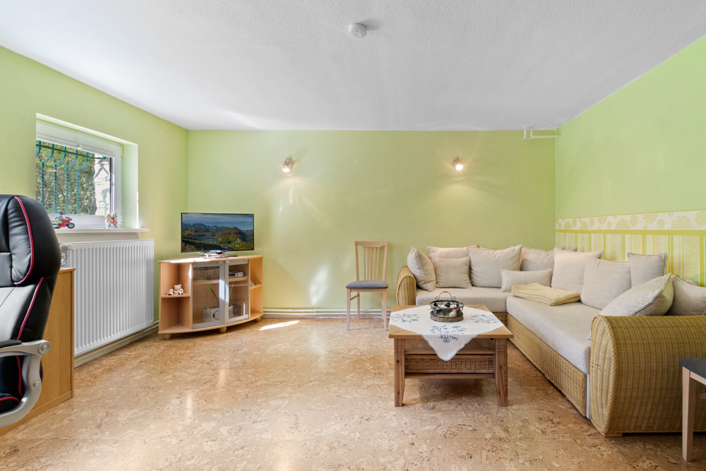 Wohnzimmer mit grün gestrichenen Wänden, Sofa, Couchtisch, Fernseher und Schreibtischstuhl.