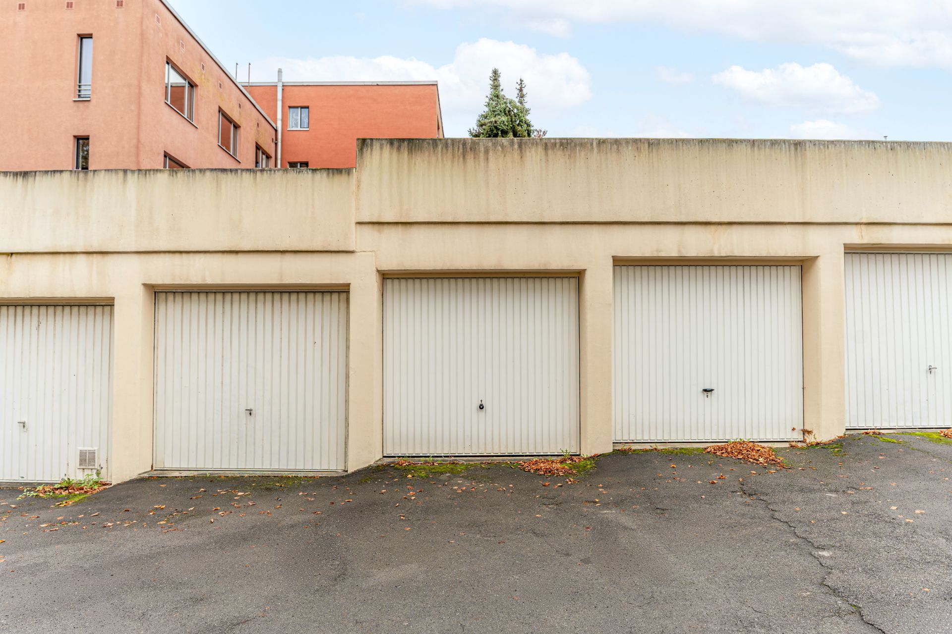 Mehrere geschlossene Garagentore vor einem Wohngebäude mit Asphaltfläche davor.