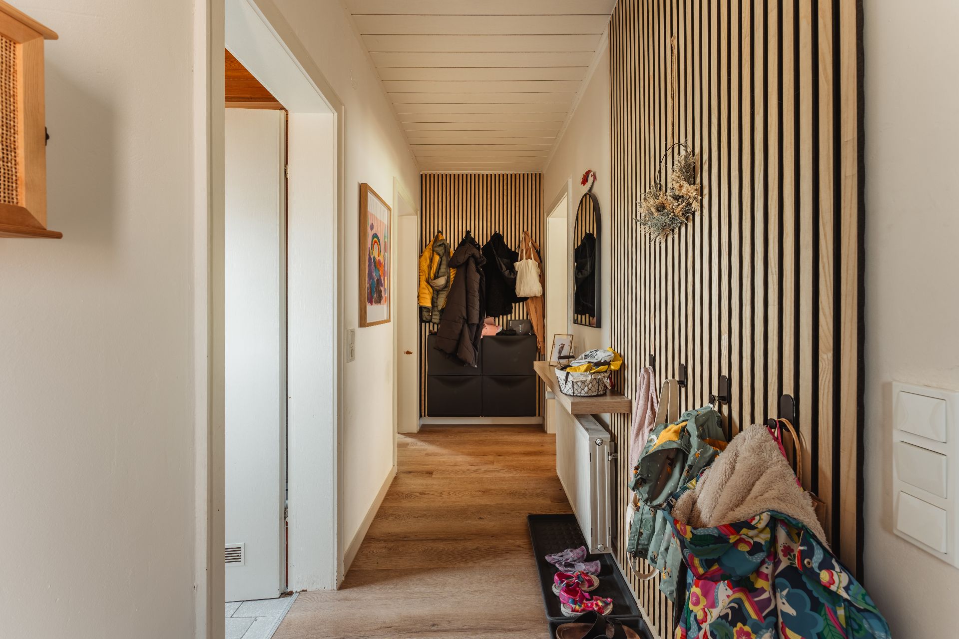 Flur einer Wohnung mit Holzboden, Garderobe, Spiegel und Haken für Jacken und Taschen.