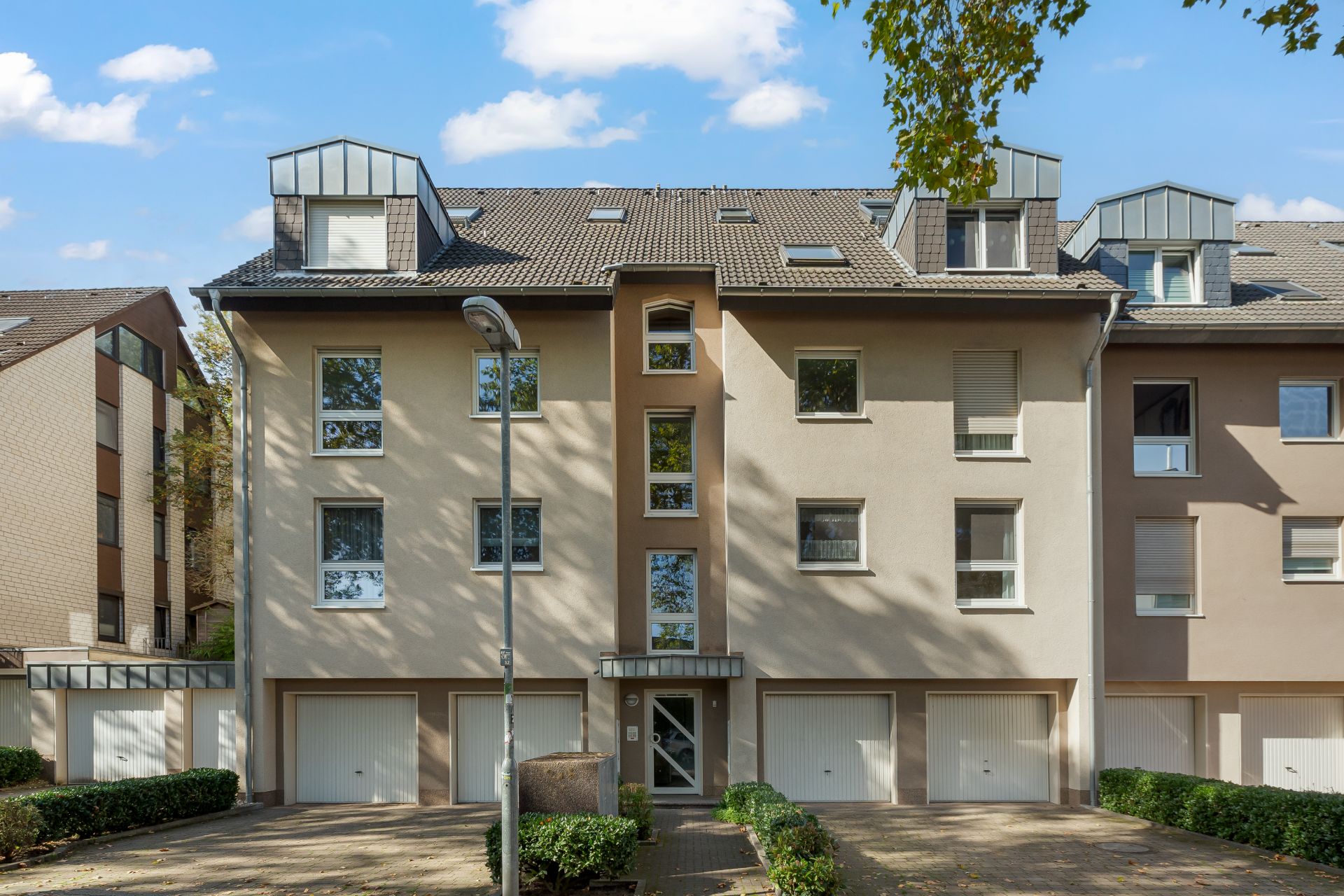 Mehrfamilienhaus mit vier Stockwerken, Dachfenstern und drei Garagen im Erdgeschoss.