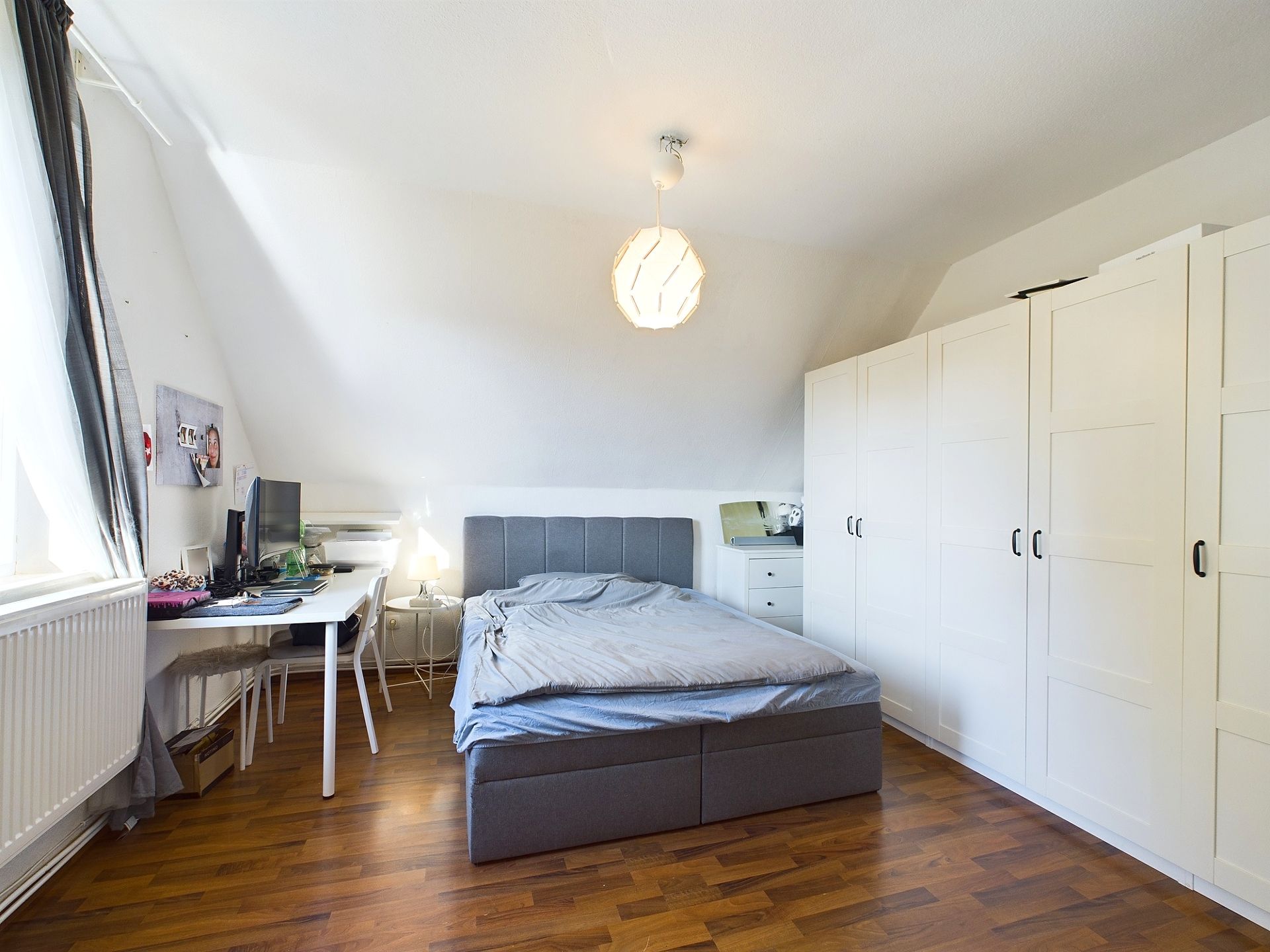 Helles Schlafzimmer mit großem Bett, weißen Schränken und Schreibtisch am Fenster.