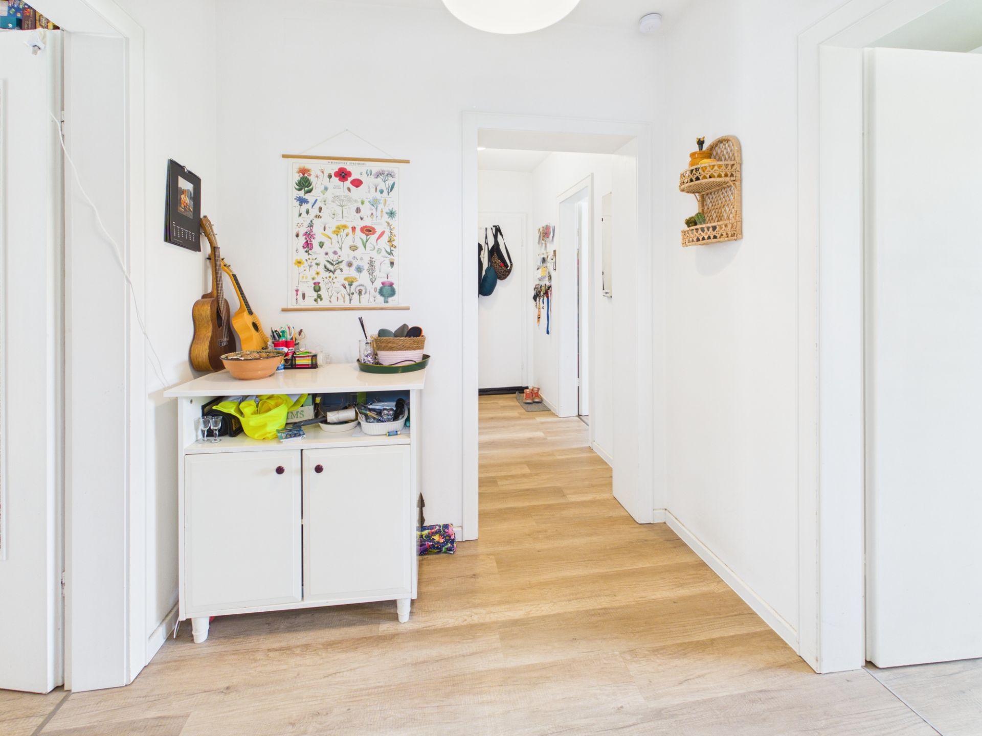 Heller Flur mit Holzboden, weißem Schrank, Wanddeko und offenem Durchgang.