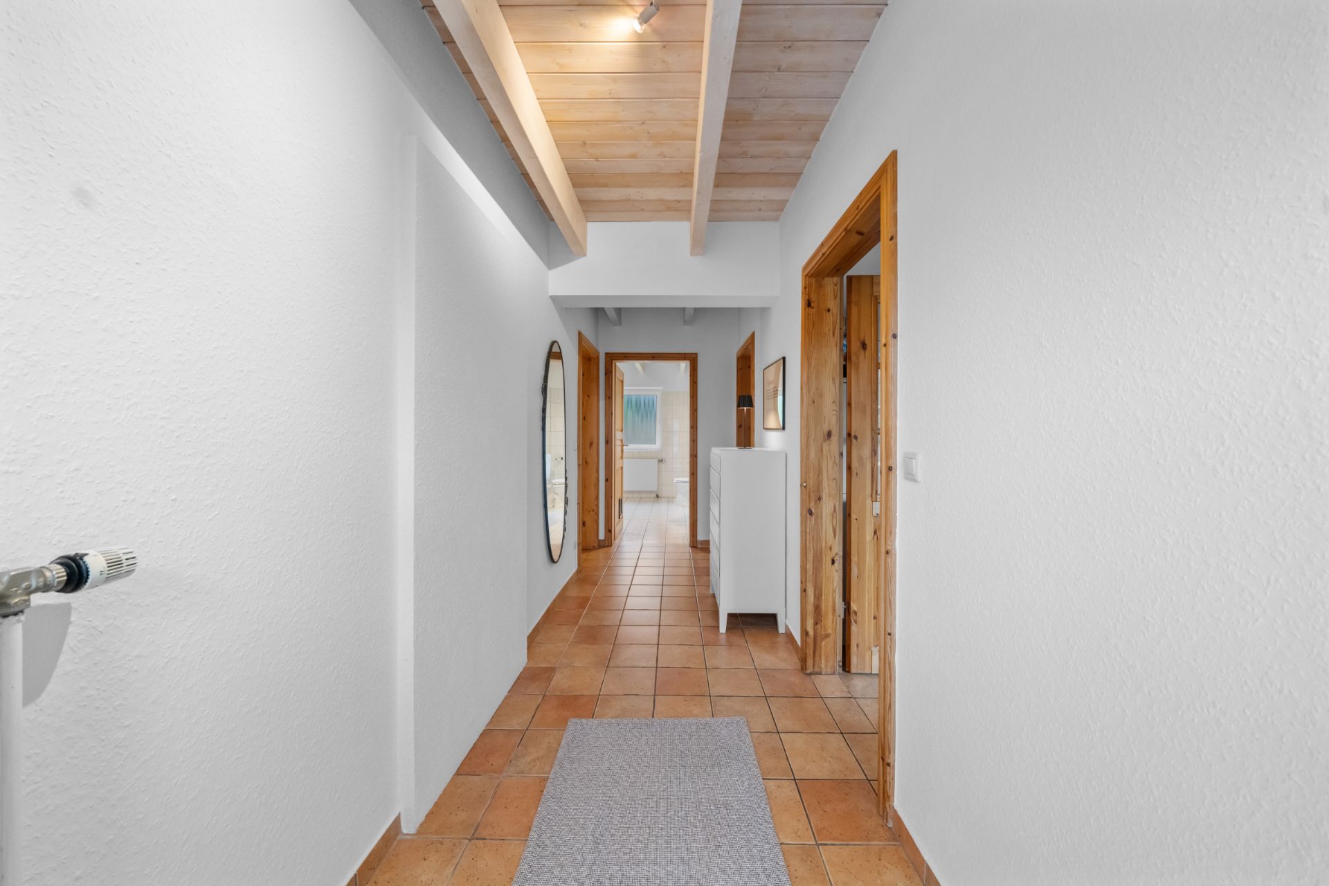 Heller Flur mit Fliesenboden, Holzdecke und mehreren Türen zu angrenzenden Räumen.