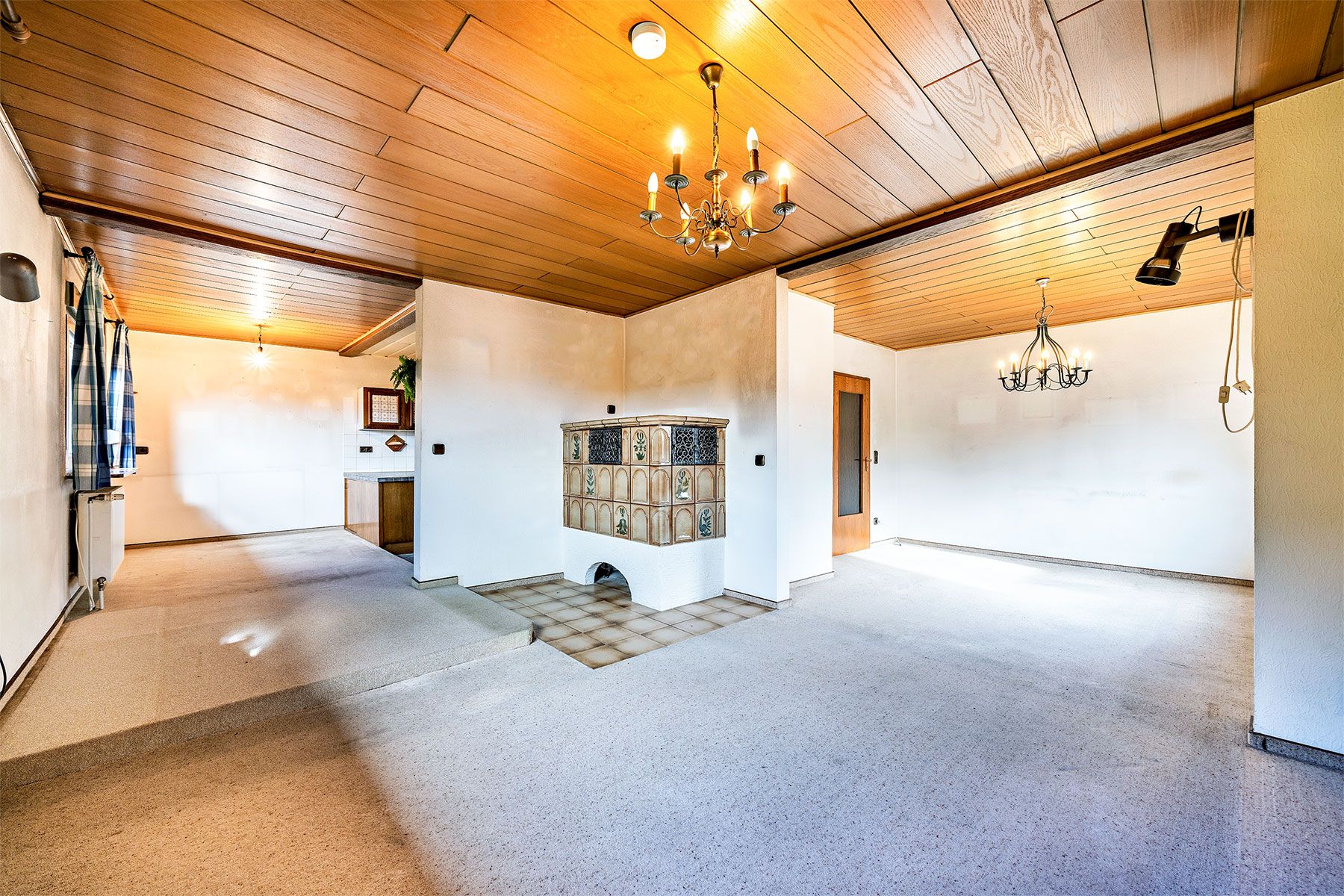 Helles Wohnzimmer mit Holzdecke, Kaminofen, Kronleuchtern und Teppichboden.
