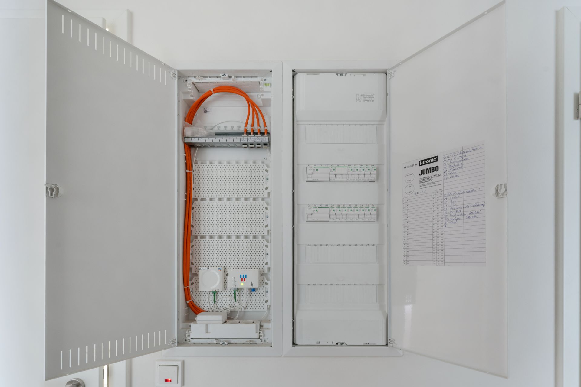 Offene Elektroverteilerkästen mit orangen Kabeln und Schaltplänen an der Wand.