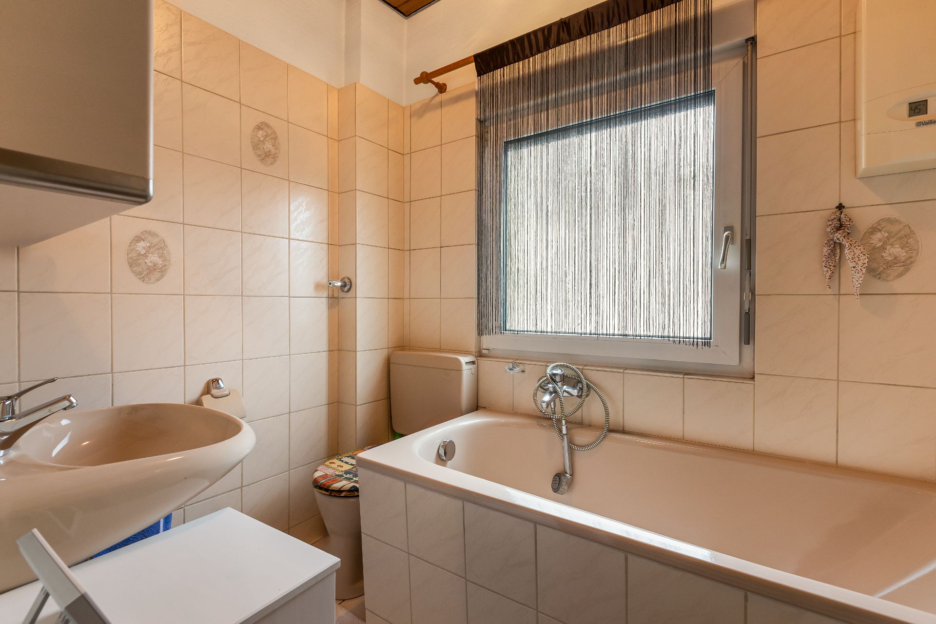 Badezimmer mit Badewanne, Waschbecken, Toilette und großem Fenster mit Vorhang.