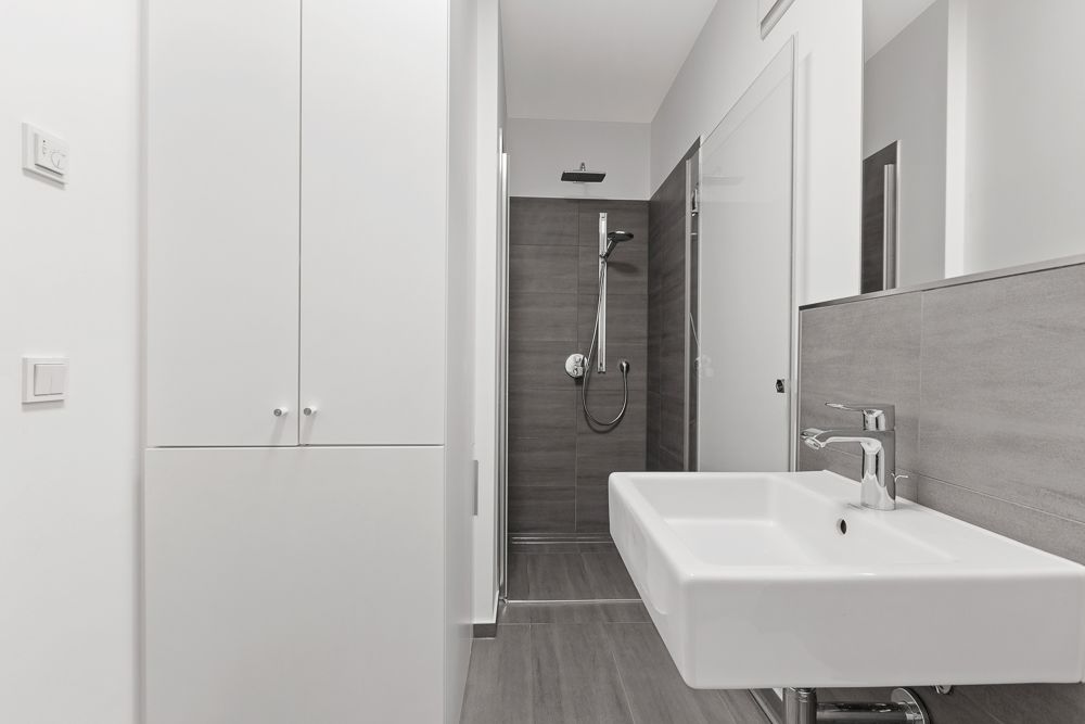 Modernes Badezimmer mit großem Waschbecken, grauen Fliesen und einer begehbaren Dusche.