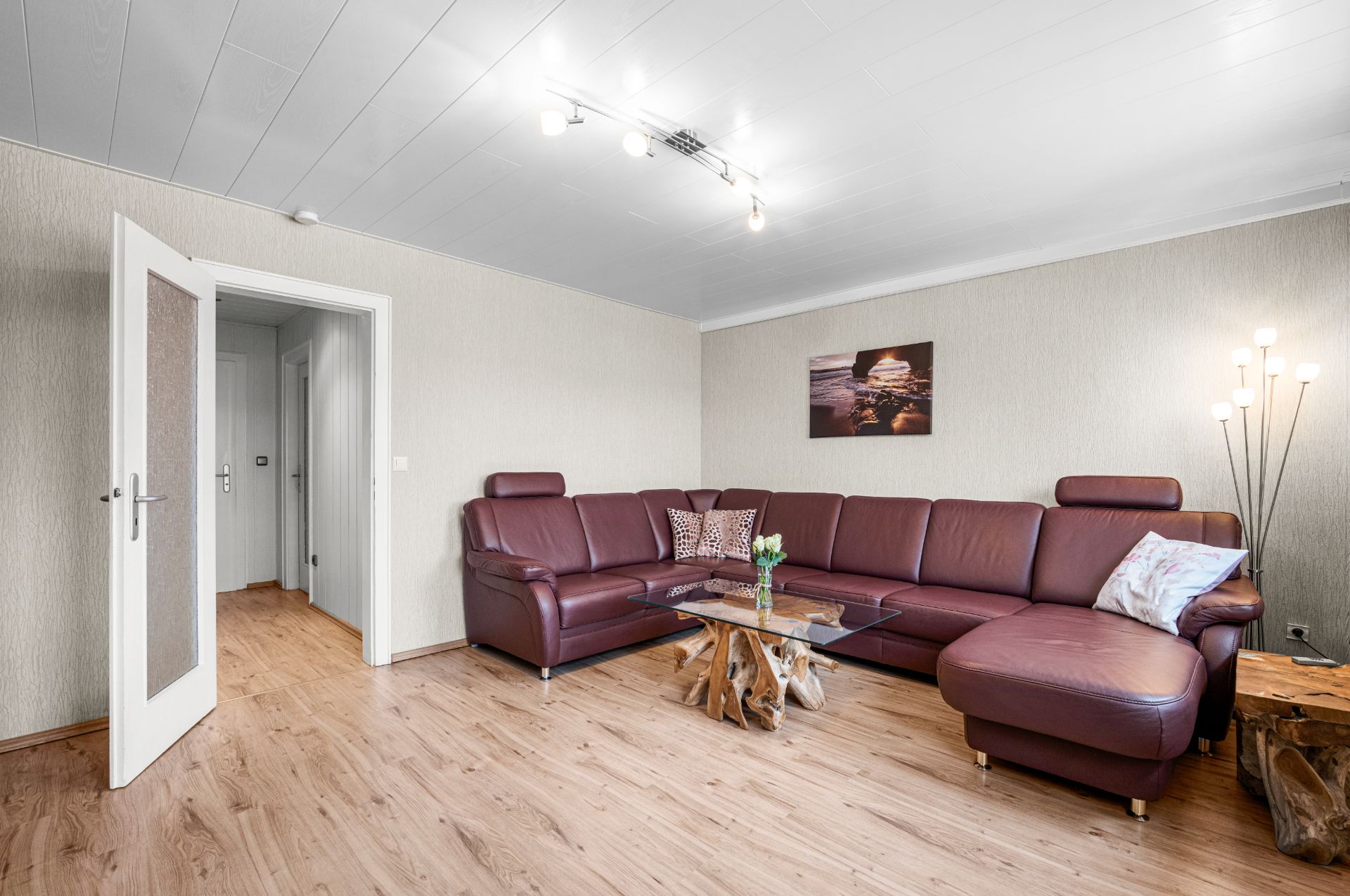 Wohnzimmer mit brauner Eckcouch, Glastisch, Holzfußboden und Wandbild.