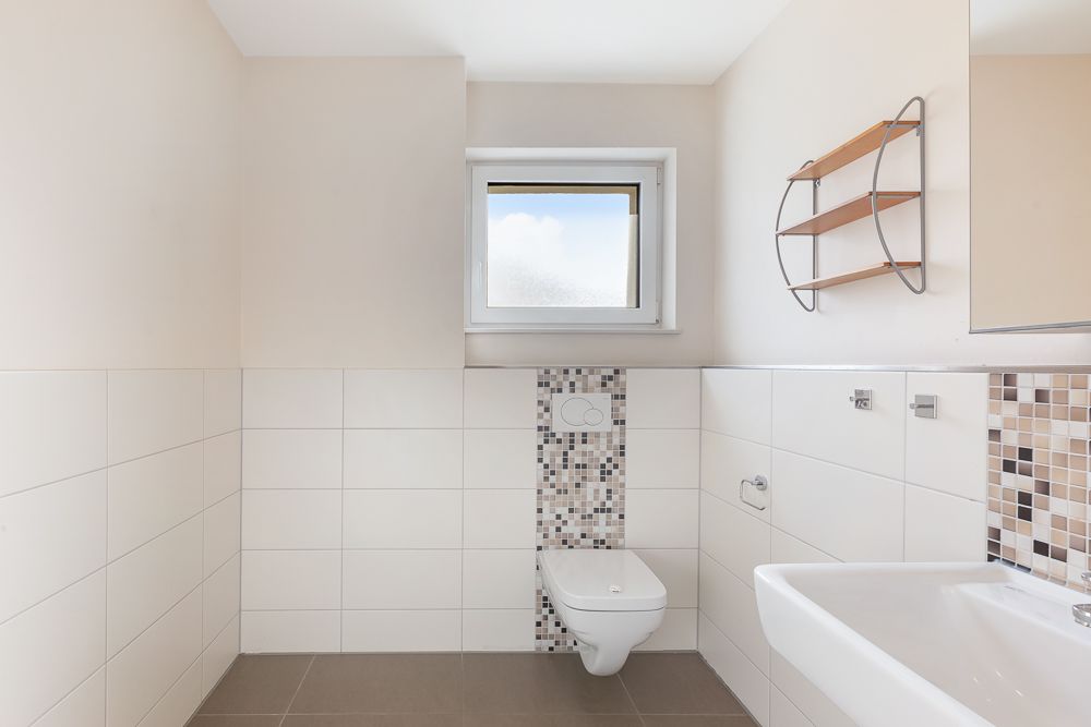 Modernes Badezimmer mit Wandtoilette, Waschbecken, kleinem Fenster und Regal an der Wand.