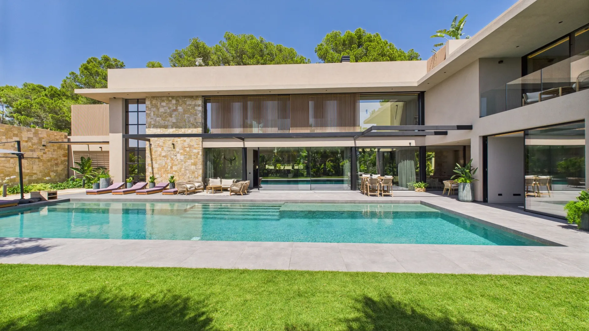 Moderne Villa mit großem Pool, Liegestühlen und Garten im Vordergrund.