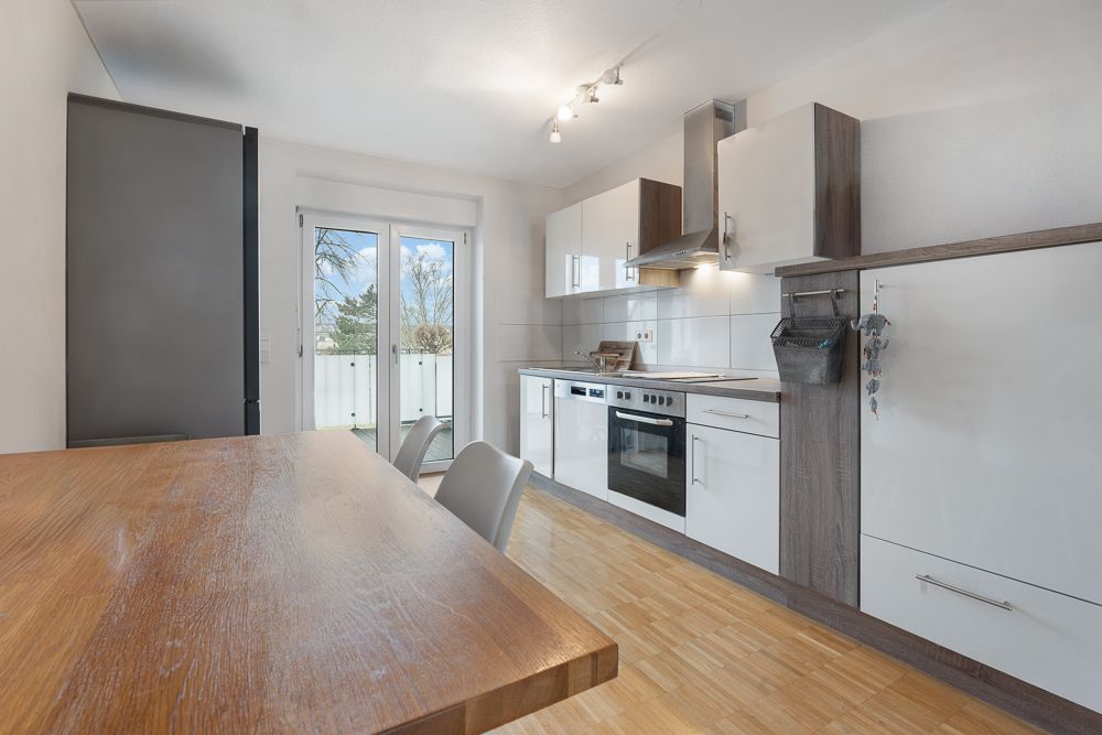 Moderne Küche mit Holztisch, weißen Schränken und Zugang zu einem Balkon durch Glastüren.