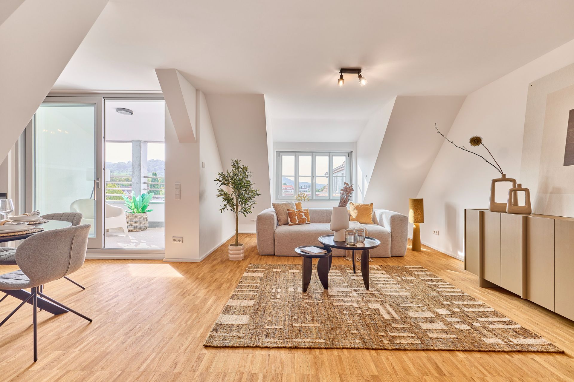Helles Wohnzimmer mit Sofa, Teppich, Couchtischen und Zugang zu Balkon, mit Esstisch links.