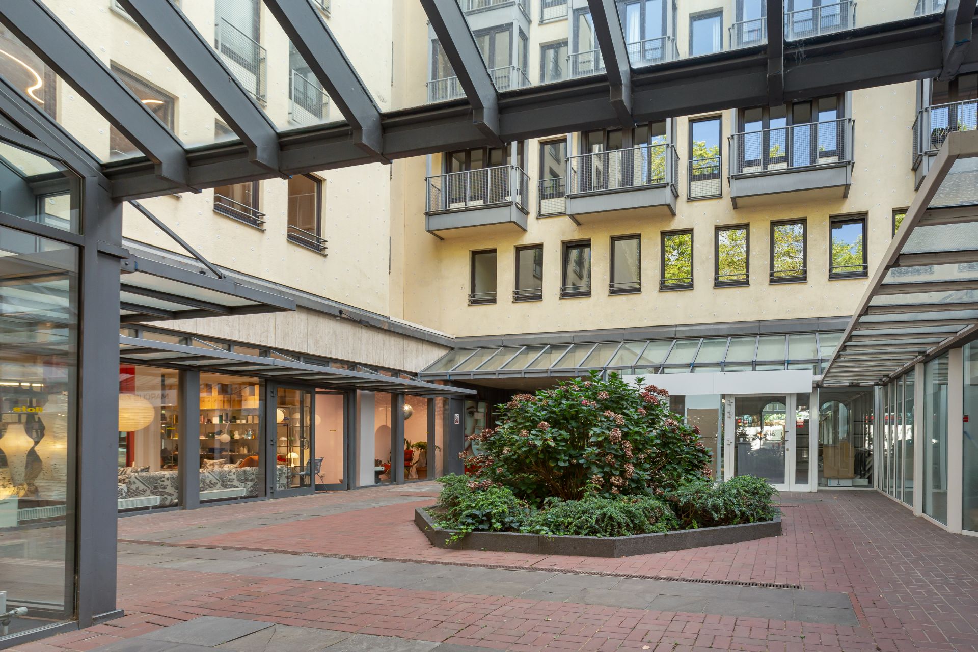 Innenhof eines Wohngebäudes mit Glasdach, Pflanzenbeet und umliegenden Fenstern.