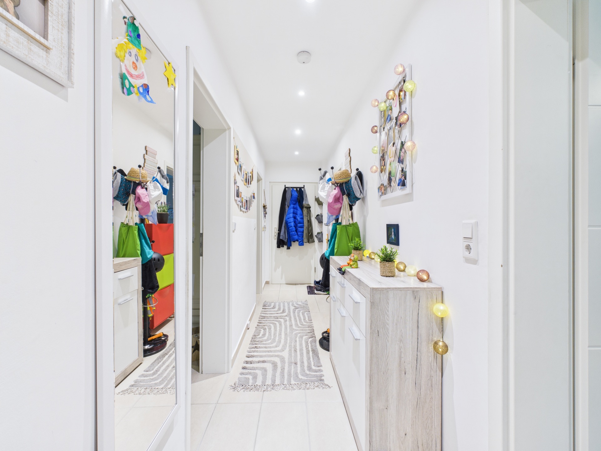 Heller Flur mit Garderobe, Kommode, Spiegel und bunter Dekoration an den Wänden.