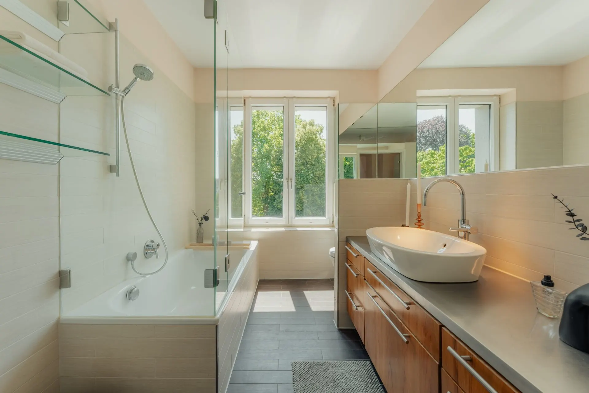 Modernes Badezimmer mit Badewanne, Dusche, großem Waschbecken und Fenster mit Blick ins Grüne.