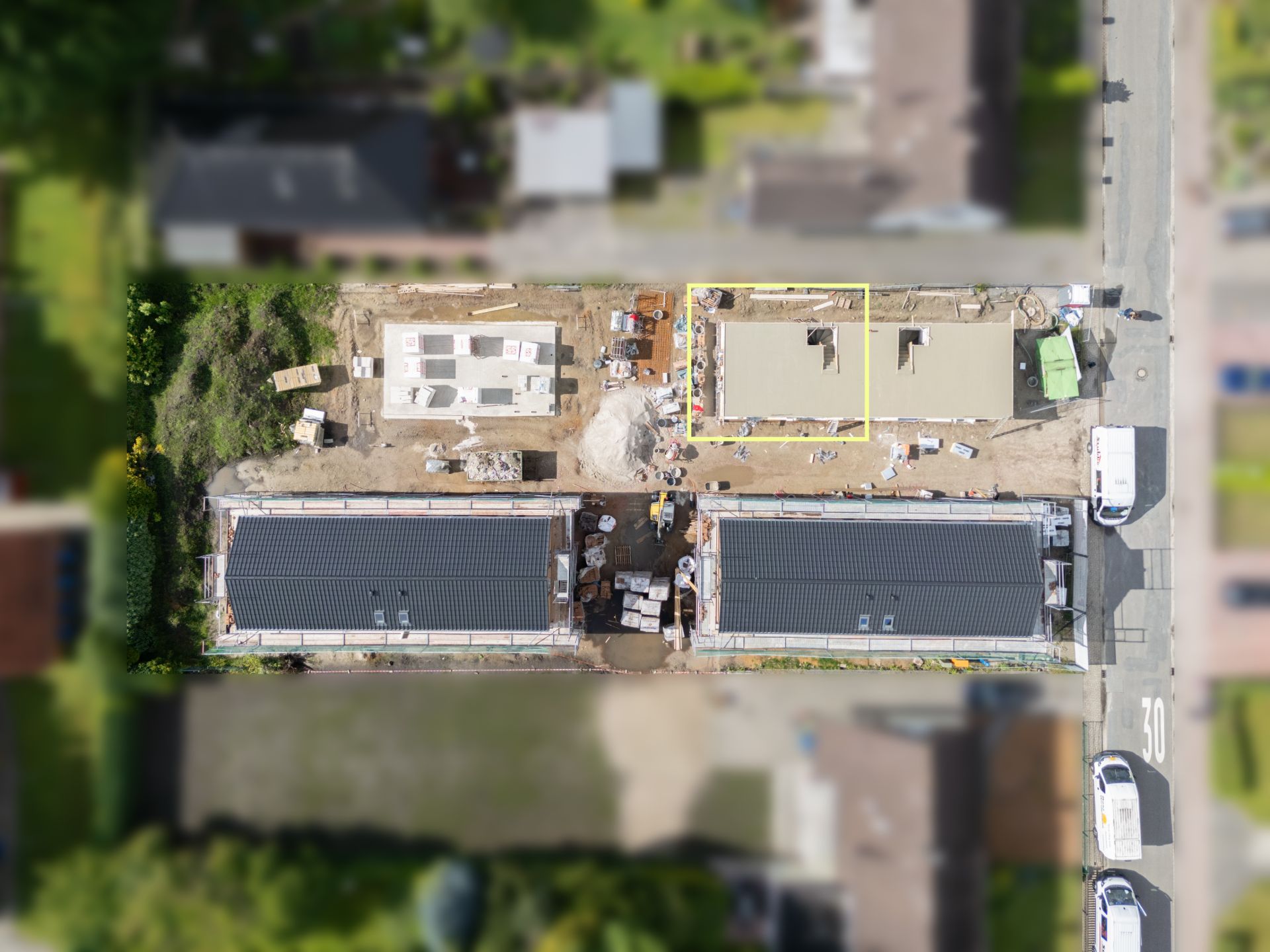 Luftaufnahme einer Wohnbaustelle mit zwei Gebäuden und Baumaterialien auf dem Grundstück.