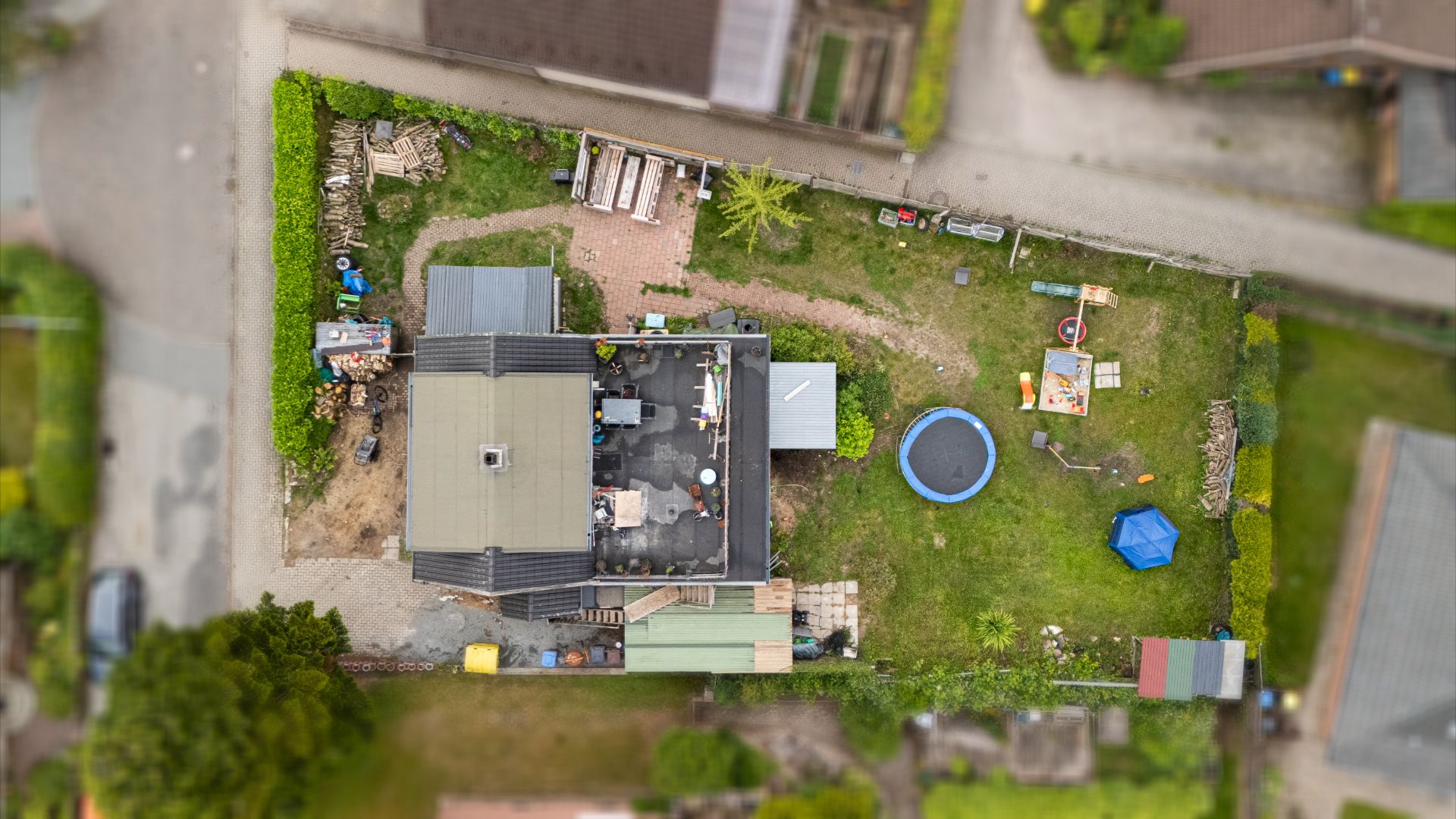 Luftaufnahme eines Hauses mit Garten, Trampolin und Sitzbereich im Hof.