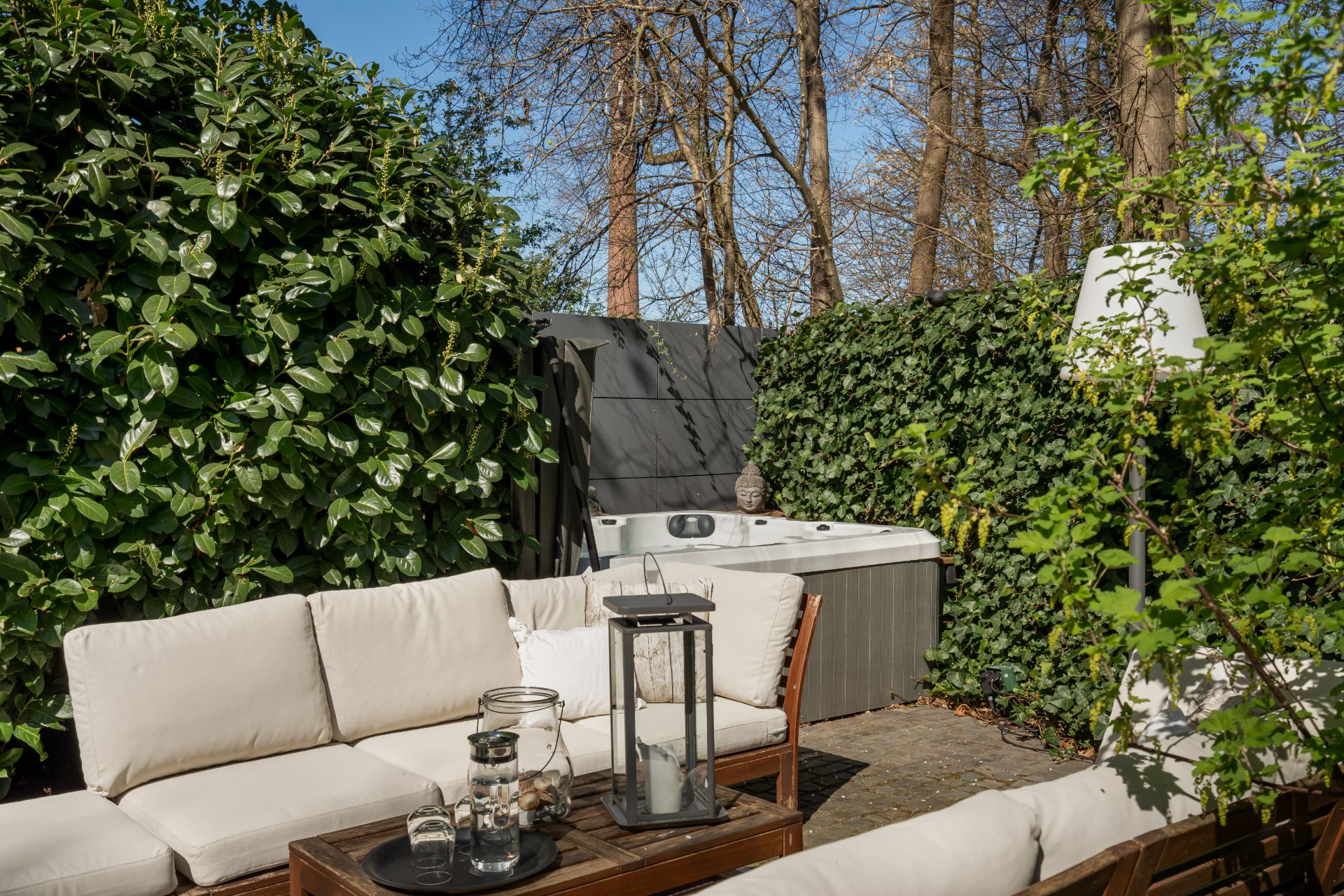 Gartenbereich mit weißen Polstermöbeln, Whirlpool und viel grüner Bepflanzung.