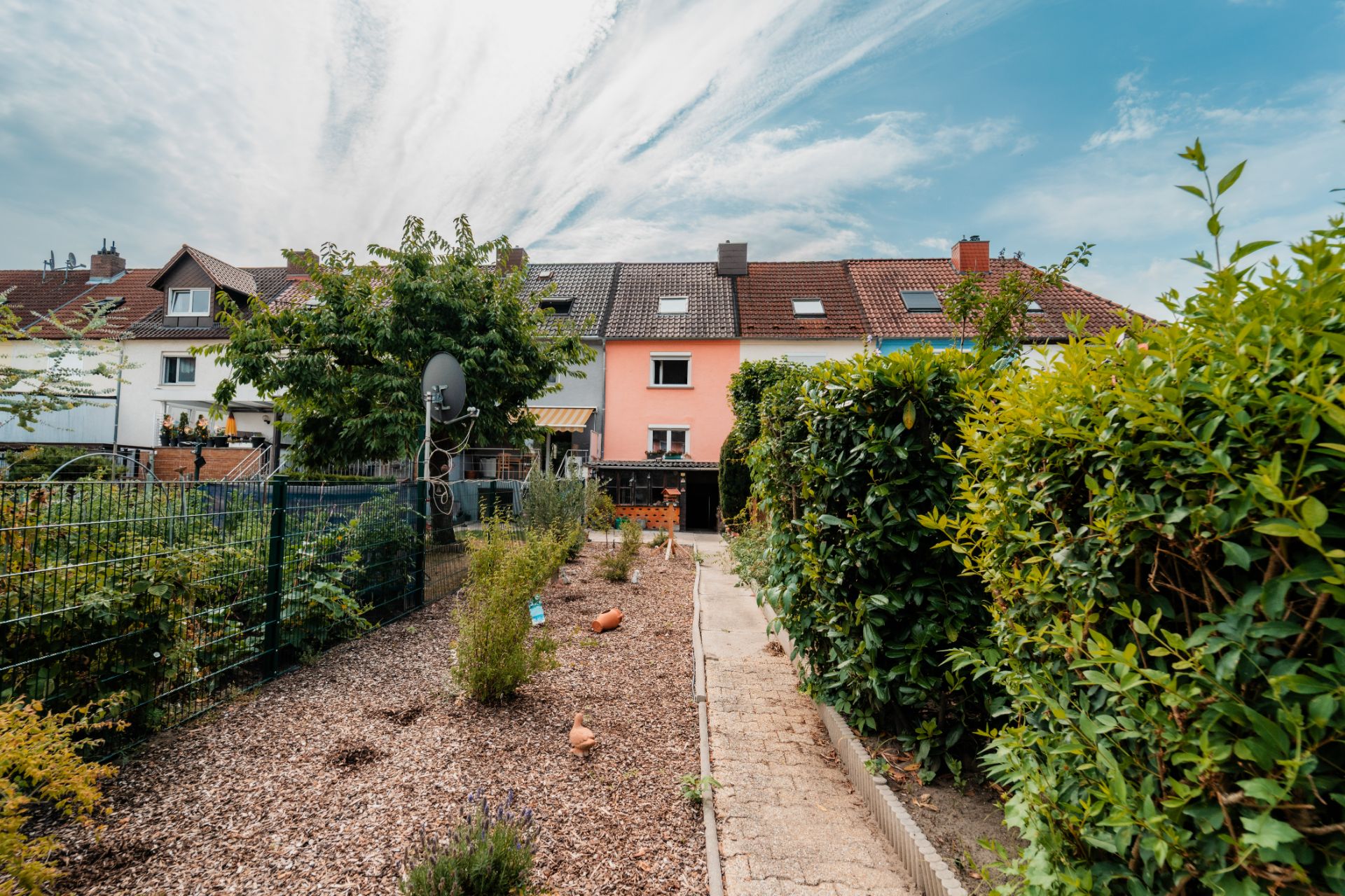 Rückansicht von Reihenhäusern mit Garten, Weg und Büschen im Vordergrund.