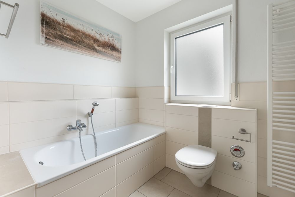 Helles Badezimmer mit Badewanne, WC, Fenster und Handtuchheizkörper.
