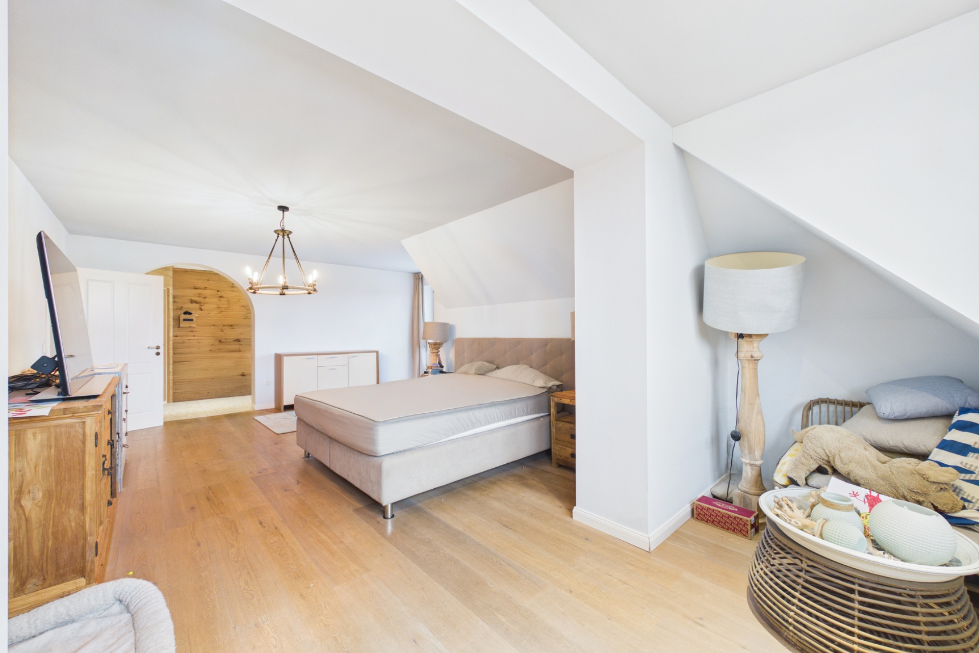 Helles Schlafzimmer mit Doppelbett, Holzboden, Kommode und Sitzbereich unter Schräge.