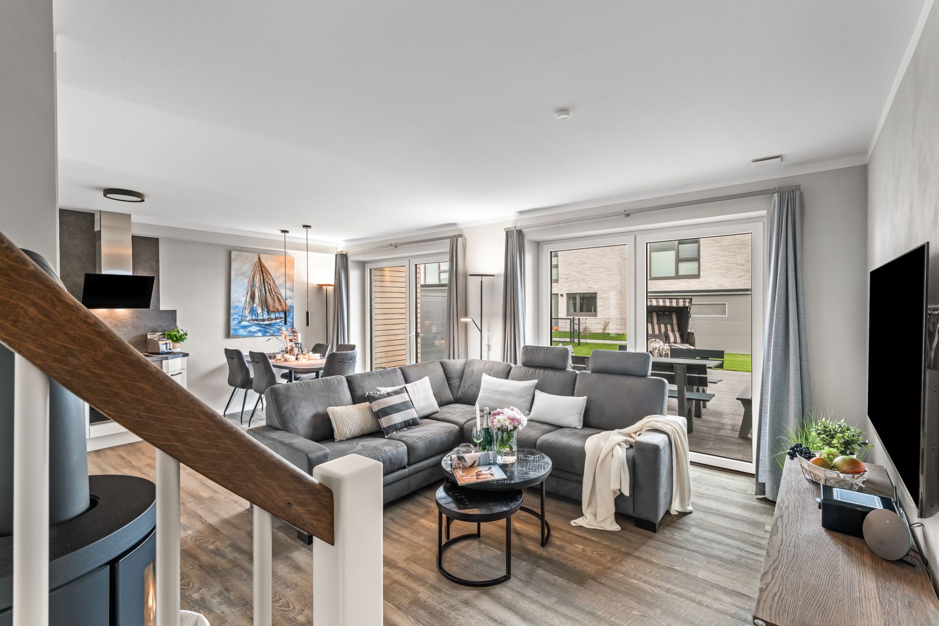 Modernes Wohnzimmer mit großer grauer Eckcouch, Esstisch und Zugang zur Terrasse mit Garten.