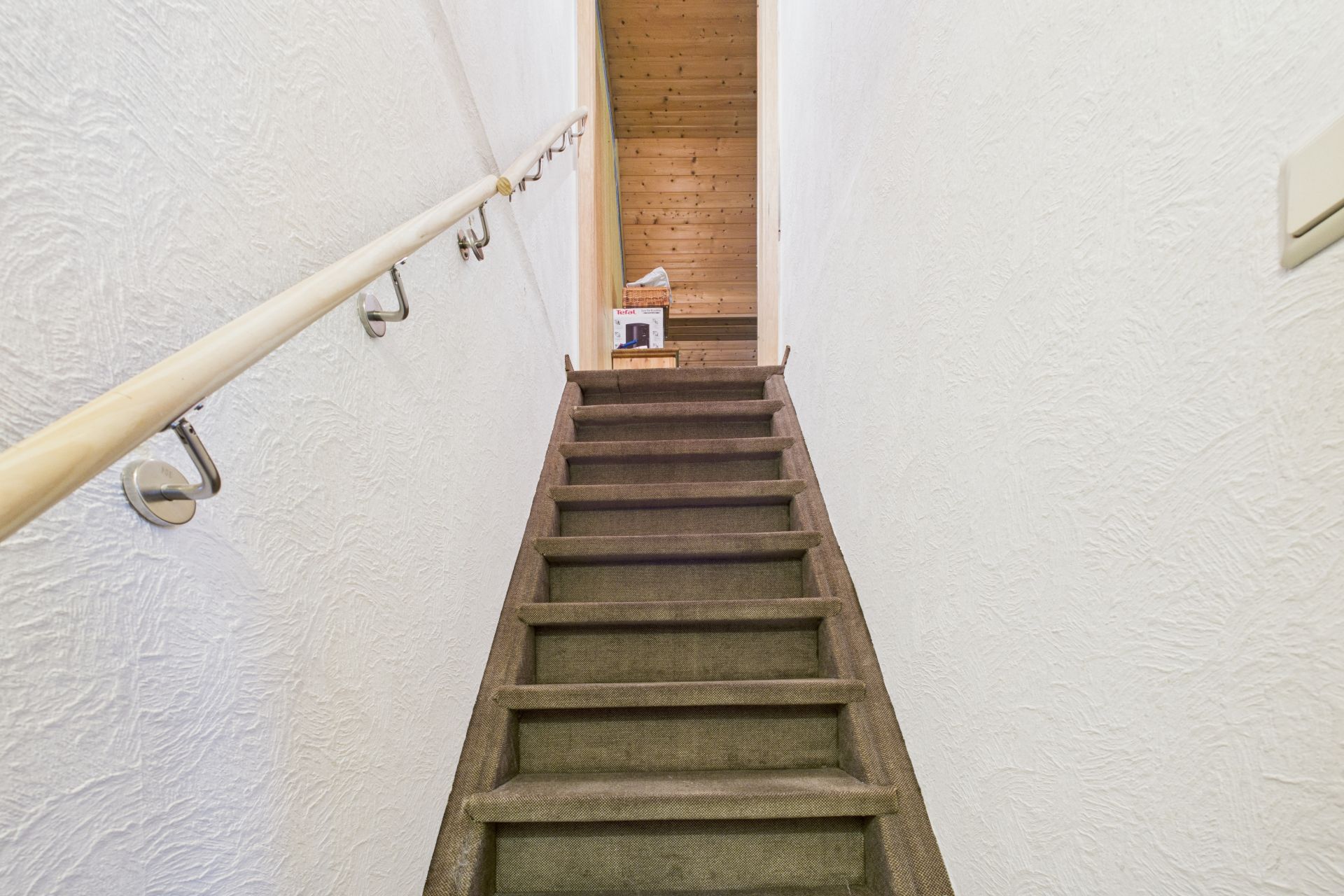 Gerade Holztreppe mit Handlauf, darüber ein Flur mit Holzverkleidung.